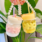 Two glass bottles with pearl rope strips and sipper straws in pink and yellow colors, held by a hand, with a pearl-embellished rope.